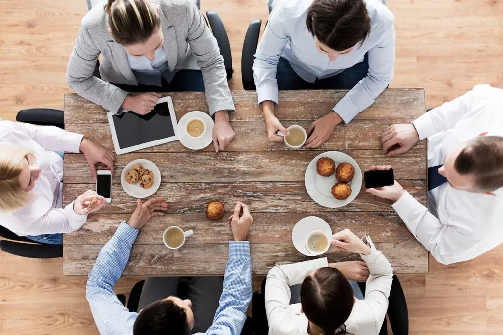 six people sitting down having a business meeting with coffee and snacks