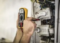 a male engineer testing an electrical fuse board with a multimeter